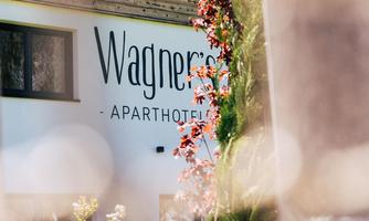 A part of the building of an aparthotel with the label "Wagner". Surrounded by plants and a soft focus.