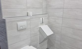 A modern bathroom with bright tiles and a white toilet. The walls are simply designed, featuring a horizontal stone line.