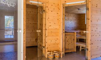 A bright sauna with wooden walls and seating. In the foreground, there are two buckets waiting for the sauna experience.