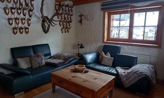 A cozy living room with a blue sofa and a wooden table. Antler pieces hang on the walls, and a window provides daylight.