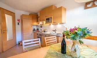 A modern kitchen with wooden cabinets and a bright decor. On the table are a bottle of wine and a bouquet of flowers.