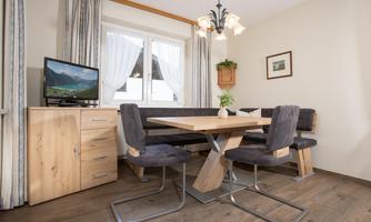 A cozy dining area with a wooden round table and modern chairs. The windows let in plenty of light and the room is tastefully decorated.