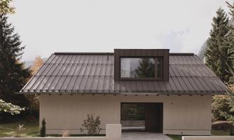 A modern house with a sloped, metallic roof. Surrounded by trees and a well-kept garden.
