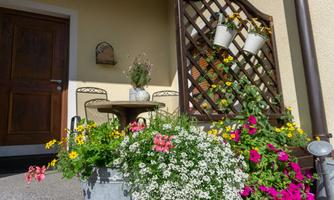 An inviting entrance area with colorful potted flowers. A small table with chairs and a wooden slat wall complete the cozy atmosphere.