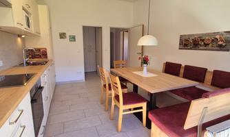A modern kitchen with a cozy dining area. The table is made of wood and surrounded by chairs with red upholstery.