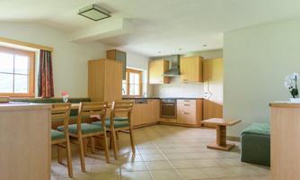 A modern kitchen with wooden cabinets and a dining area. The room is bright and friendly, with large windows and a cozy atmosphere.