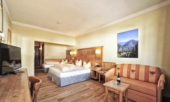 A cozy hotel room with two beds and a sofa. The walls are painted in soft colors and a picture of a mountain landscape hangs on the wall.