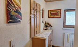 A cozy hallway with a wooden cabinet and decorative pictures on the wall. On the side, there is a flower arrangement and a mirror.