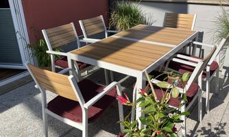 A modern table with six chairs is set in a bright outdoor area. Surrounded by plants and sunlight, the space invites outdoor dining.