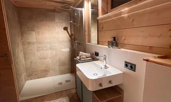 A modern bathroom with wooden details. There is a shower, a sink, and a large mirror.
