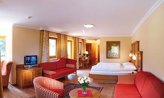 A bright room with two red sofas and a table. There is a comfortable bed and windows that let in a lot of daylight.