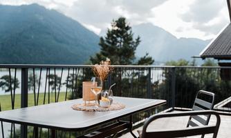 A cozy balcony with a table and chairs, decorated with a great arrangement. In the background, mountains and a beautiful lake can be seen.