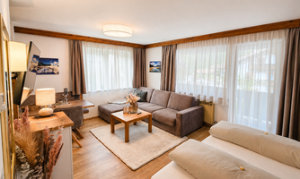 A cozy living area with a gray sofa and a wooden table. Large windows provide plenty of daylight and an inviting atmosphere.