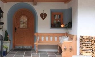A cozy entryway with a wooden bench and a round wooden door. The walls are painted light, and a small windowsill is decorated with plants.