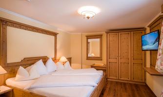 A cozy bedroom with wooden furniture and a large double bed. There is a television, a mirror, and a wooden wardrobe.