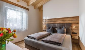 A modern bedroom with a double bed and wooden walls. The windows let in a lot of light, and a vase with flowers adds a fresh touch.