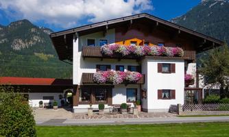 A beautiful house with balconies adorned with blooming plants. In the background, mountains and a clear blue sky are visible.