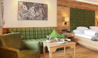 A cozy room with wooden paneling, a relaxation area, and a dining space. The sofa has a checkered pattern, and the wall is decorated with a green patterned fabric.