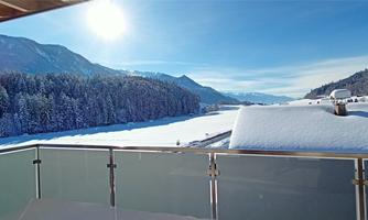 A clear winter day with snow-covered mountains and trees. The sun shines over the snowy landscape.