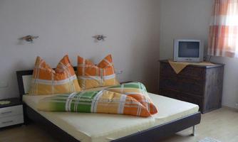 A bright bedroom with a large bed and colorful cushions. A television and a wooden furniture piece are also visible in the room.
