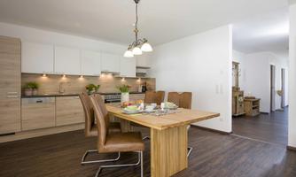 A modern kitchen with a dining table and chairs. There is a bright wood design and a simple, friendly atmosphere.