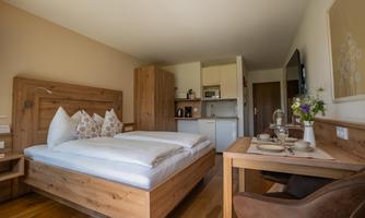 A cozy room with a large bed and wood grain. There is a small kitchenette and a dining area with a table.