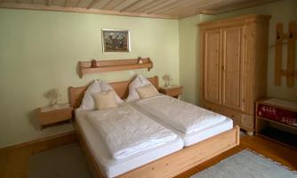 A cozy bedroom with two single beds and wooden furniture. The walls are painted in light green and there are decorative elements like a picture and a carpet.