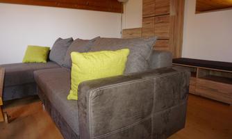 A modern living room with a comfortable gray couch and a bright yellow cushion. In the background, wooden shelves can be seen.
