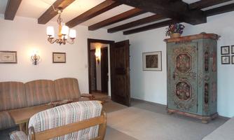 A cozy living space with wooden ceiling beams and a colorful cupboard. The sofas and table are adorned with striped cushions, and a lamp provides pleasant lighting.