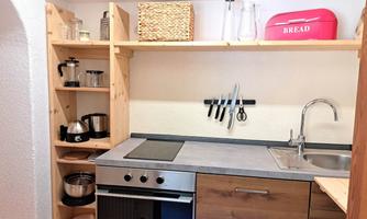 A modern kitchen with wooden shelves and a sink. Various kitchen appliances and a red bread box are on the countertop.