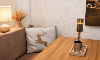 Cozy living area with a wooden table and a bench. A pillow with a deer motif and soft light from a lamp create an inviting atmosphere.