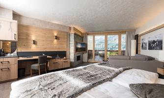 A modern room with a cozy atmosphere and wooden details. Large windows offer a beautiful view of the mountains.