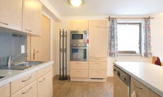 A modern kitchen with wooden cabinets and bright walls. It features a refrigerator, an oven, and a sink.