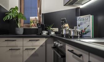 A modern kitchen with elegant black and white cabinets. On the countertop, there are pots and a cookbook, surrounded by plants and kitchen utensils.