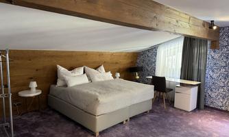 A modern bedroom with a large bed and many pillows. The room has a cozy atmosphere with wooden details and a desk.