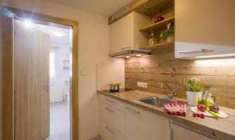 A modern kitchen with wooden shelves and bright walls. Fresh vegetables and a small cooking area can be seen on the countertop.