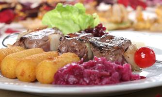 A plate with juicy meat, surrounded by crispy croquettes and a colorful beetroot puree. A leaf of lettuce and a small tomato complete the dish.