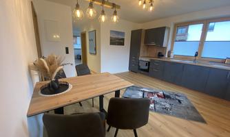 A modern kitchen with a dining area and stylish chairs. The space is bright and inviting, with wooden flooring and decorative elements.