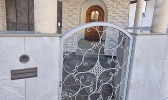 An elegant gate made of wrought iron opens to a modern entrance area. The ground is covered with a layer of snow.