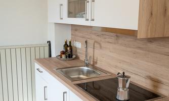 A modern kitchen with white cabinets and wood paneling. It features a sink, a cooktop, and some cooking utensils.