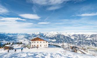 An idyllic winter landscape with snow-covered mountains and a cozy chalet. Skiers enjoy the slopes under a clear blue sky.