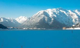 An impressive winter landscape with snow-covered mountains and a frozen lake. The clear blue sky gives the scene a peaceful atmosphere.