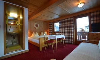 A cozy room with wood paneling and a bed. On a table, there are two chairs, and in one corner, a small bathroom is visible.
