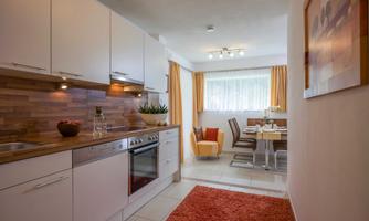 A modern kitchen with white cabinets and a wooden worktop. The dining area is bright and cheerful with a table and chairs as well as windows with curtains.