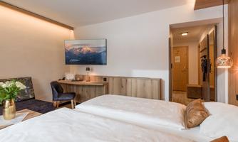 A modern hotel room with two beds and a television on the wall. A cozy seating area and elegant decor complete the space.