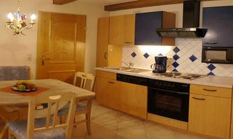 A cozy kitchen with wooden cabinets and blue accents. A dining table with chairs and decorated with fruit is also in the room.