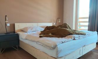 A cozy bedroom with a large bed and a warm blanket. Next to the bed is a bedside table with a modern lamp.