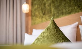 A cozy bedroom with a green pillow and warm light. The wooden details and soft colors create an inviting atmosphere.