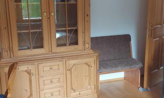 A cozy living space with a wooden display cabinet and a bench. In the background, there is a decoration in the shape of a bird hanging.