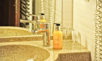 A modern sink with a stainless steel faucet and a bottle of shampoo. In the background, two glasses and a mirror reflection are visible.